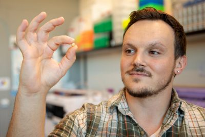 A man holds up a tiny edamame seed in front of his face.