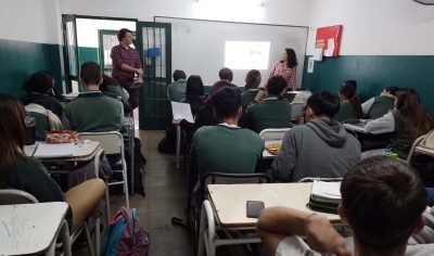 Two individuals stand at front of classroom speaking to high school students.