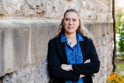 Woman stands with arms crossed next to building covered in Hokie Stone